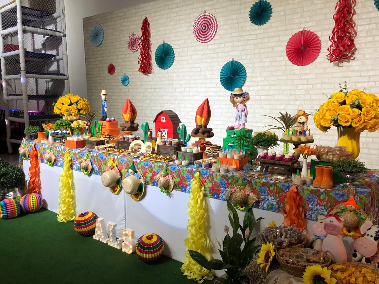 Mesa de festa junina com leques coloridos, fogueira decorativa e chapéus de palha